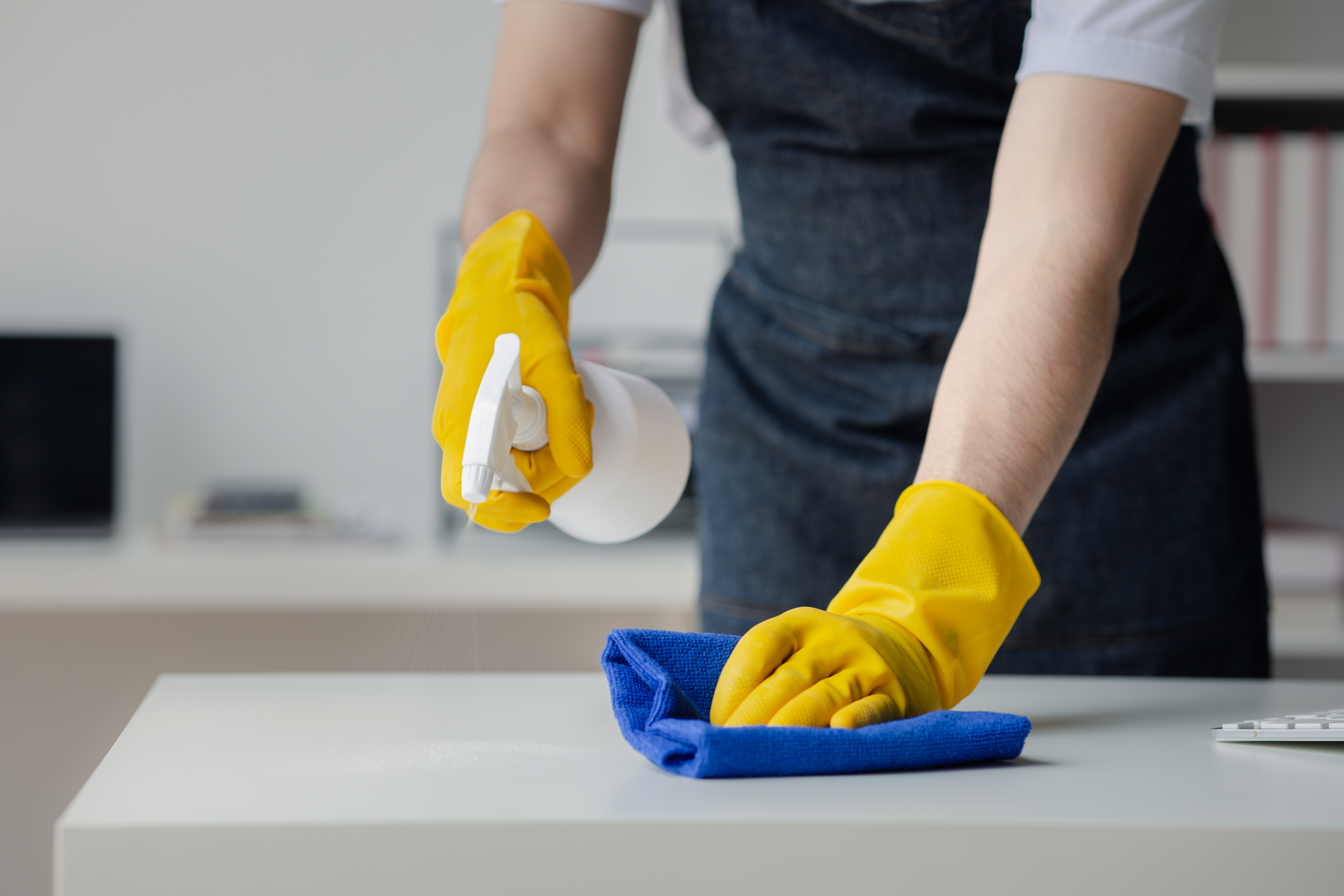 Person cleaning the room, cleaning staff is using cloth and spraying disinfectant to wipe the tables in the company office room. Cleaning staff. Maintaining cleanliness in the organization.